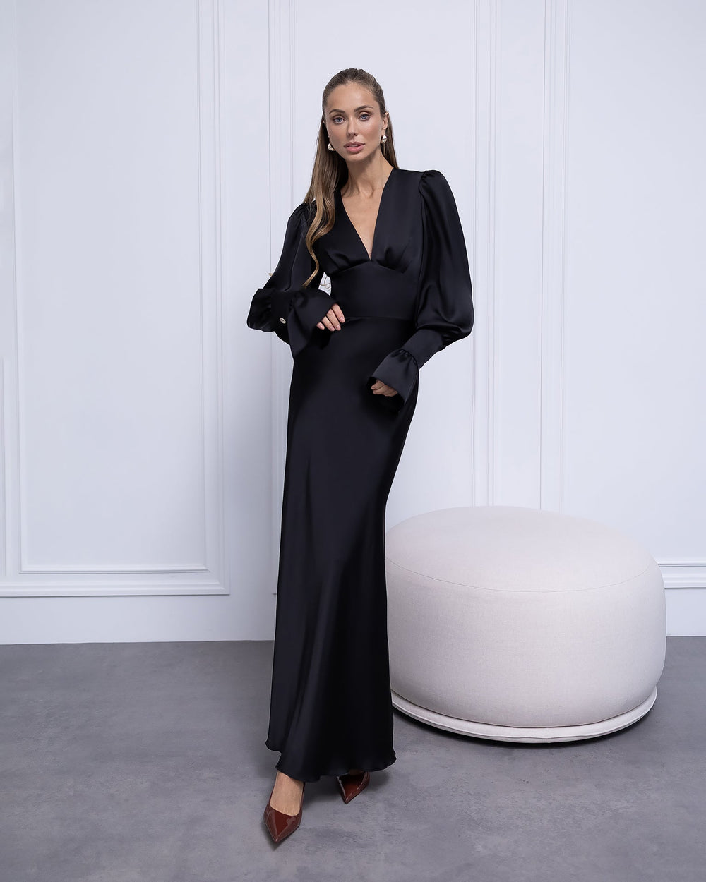 Woman in a black evening gown standing against a white paneled wall.